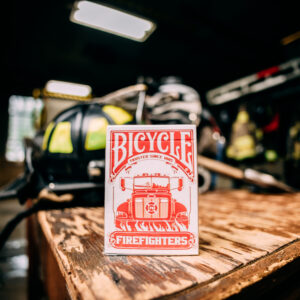 Bicycle Firefighters Playing Cards Deck on a wooden table inside of a fire station. Fire gear can be seen blurred in the background.