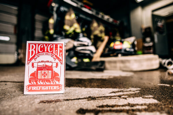 Bicycle Firefighters Playing Cards Deck on a cement floor inside of a fire station. Fire gear can be seen blurred in the background.