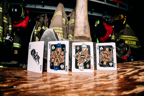 Bicycle Firefighters Playing Cards Court Cards on a wooden table inside of a fire station. Fire gear can be seen blurred in the background.