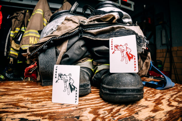 Bicycle Firefighters Playing Cards Jokers on a wooden table on the boots of turnout gear inside of a fire station. Fire gear can be seen blurred in the background.